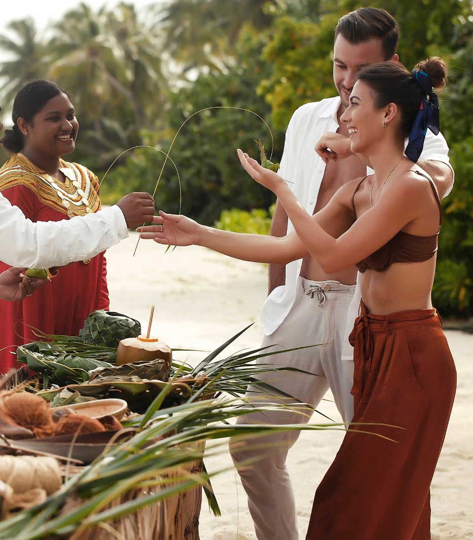 A host in a traditional Dhivehi Libaas shows guests coconut-palm weaving on the beach at Alila Kothaifaru Maldives