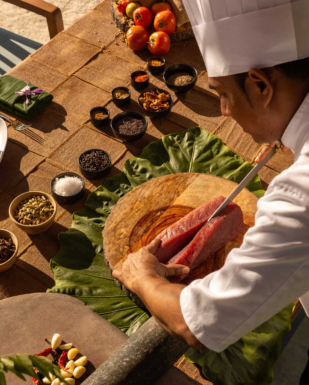 A chef slices fresh tuna on a wooden board surrounded by bowls of spices at Sun Siyam Vilu Reef Maldives