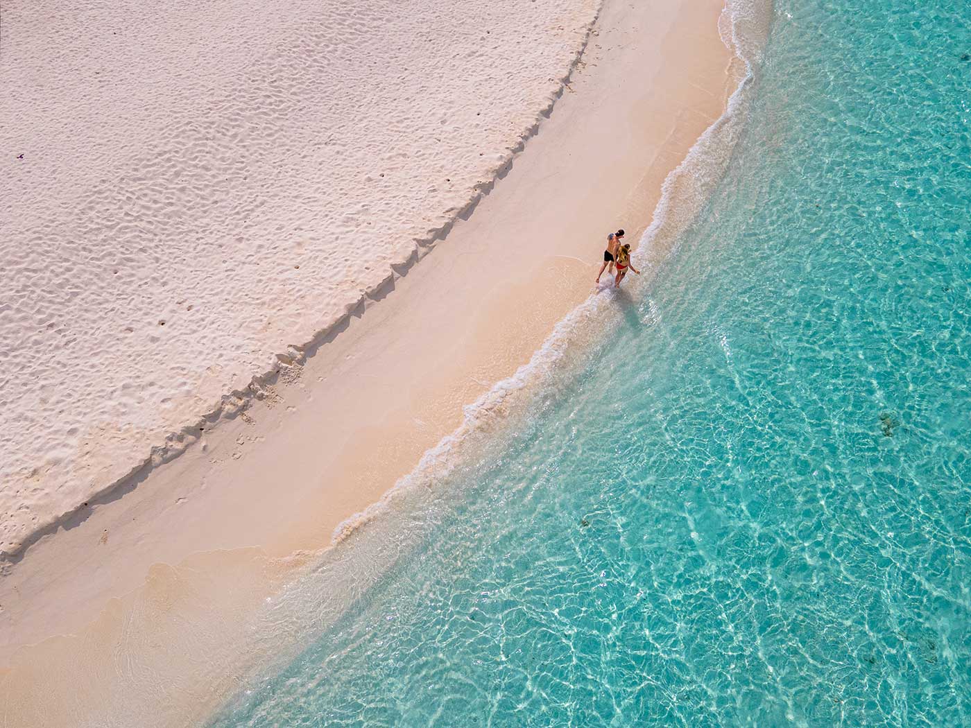 Aerial view of a couple walking where white sand meets turquoise water